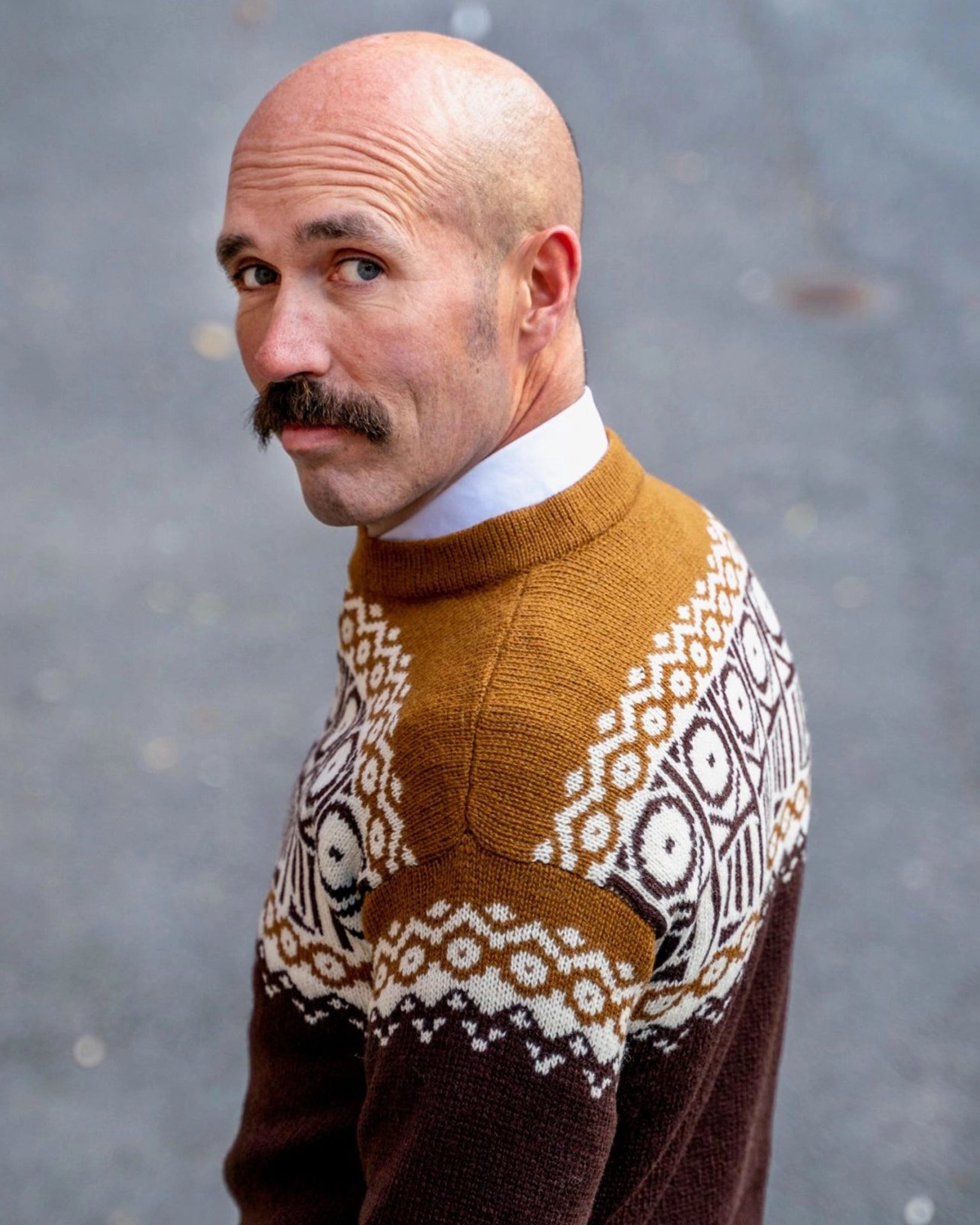 Mann i strikket Kaizers Orchestra-genser fra Vikingstrikk, i varme brun- og okertoner med naturhvitt mønster inspirert av mariusgenseren. Tradisjon.