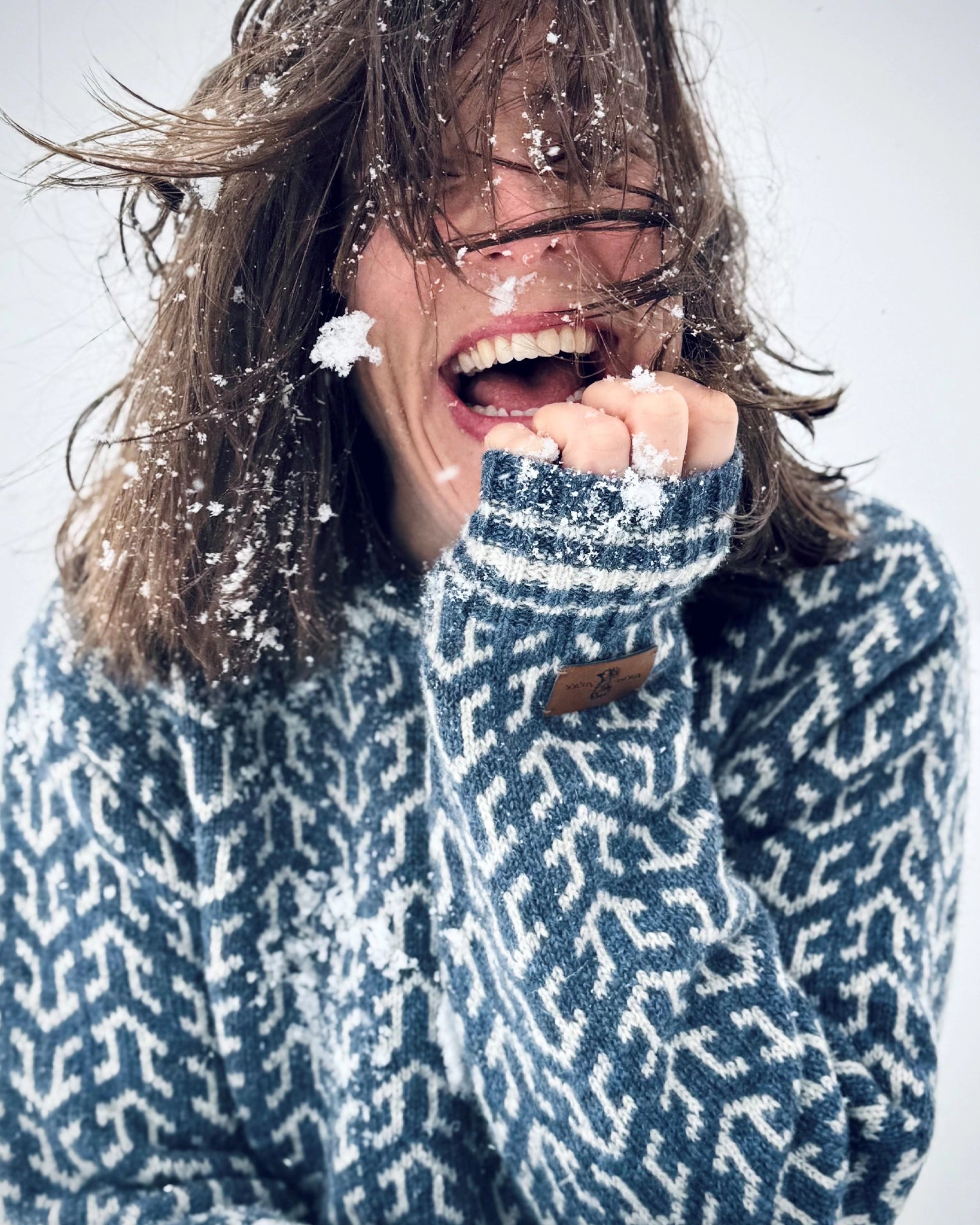 Smilende kvinne i blå og hvit Nordvegr-genser fra Vikingstrikk, en allsidig ullgenser for friluftsliv, lek, utendørs glede og byturer.