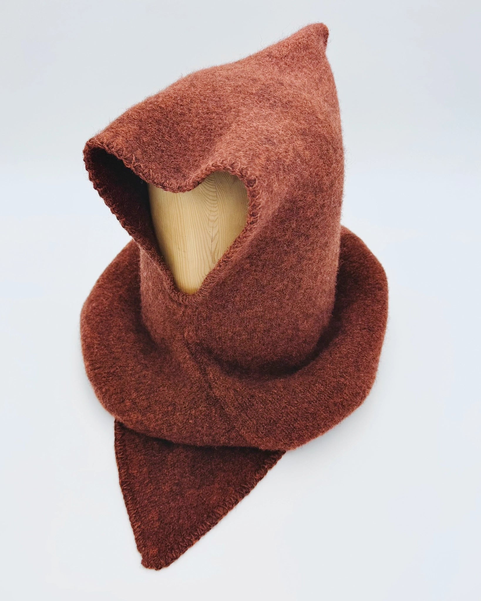 Produktfoto av rustrød Vikinghette fra Vikingstrikk, laget i myk ull med spiss hette og bred skulderkrage.