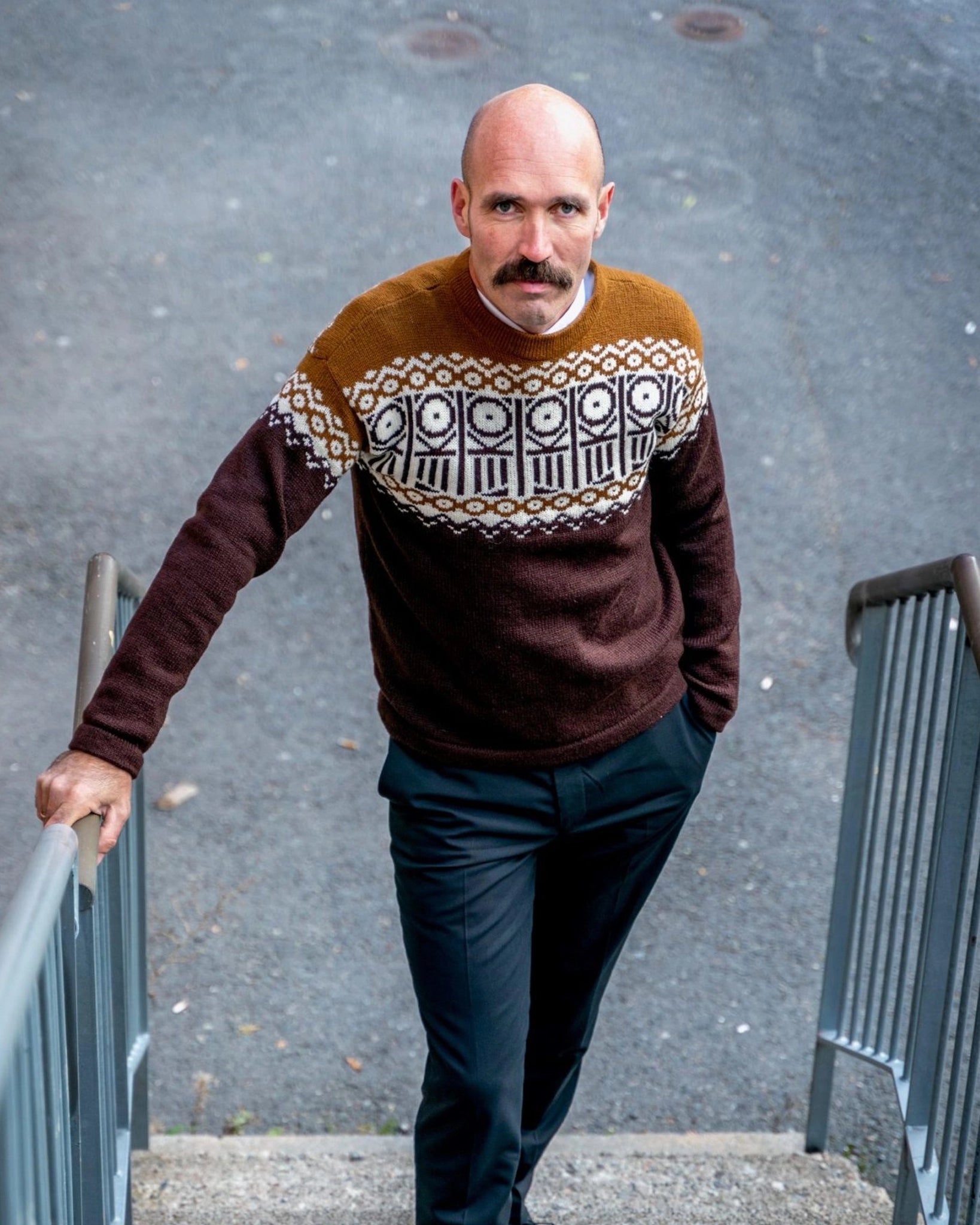 Mann i strikket Kaizers Orchestra-genser fra Vikingstrikk, i varme brun- og okertoner med naturhvitt mønster inspirert av mariusgenseren. Tradisjon.