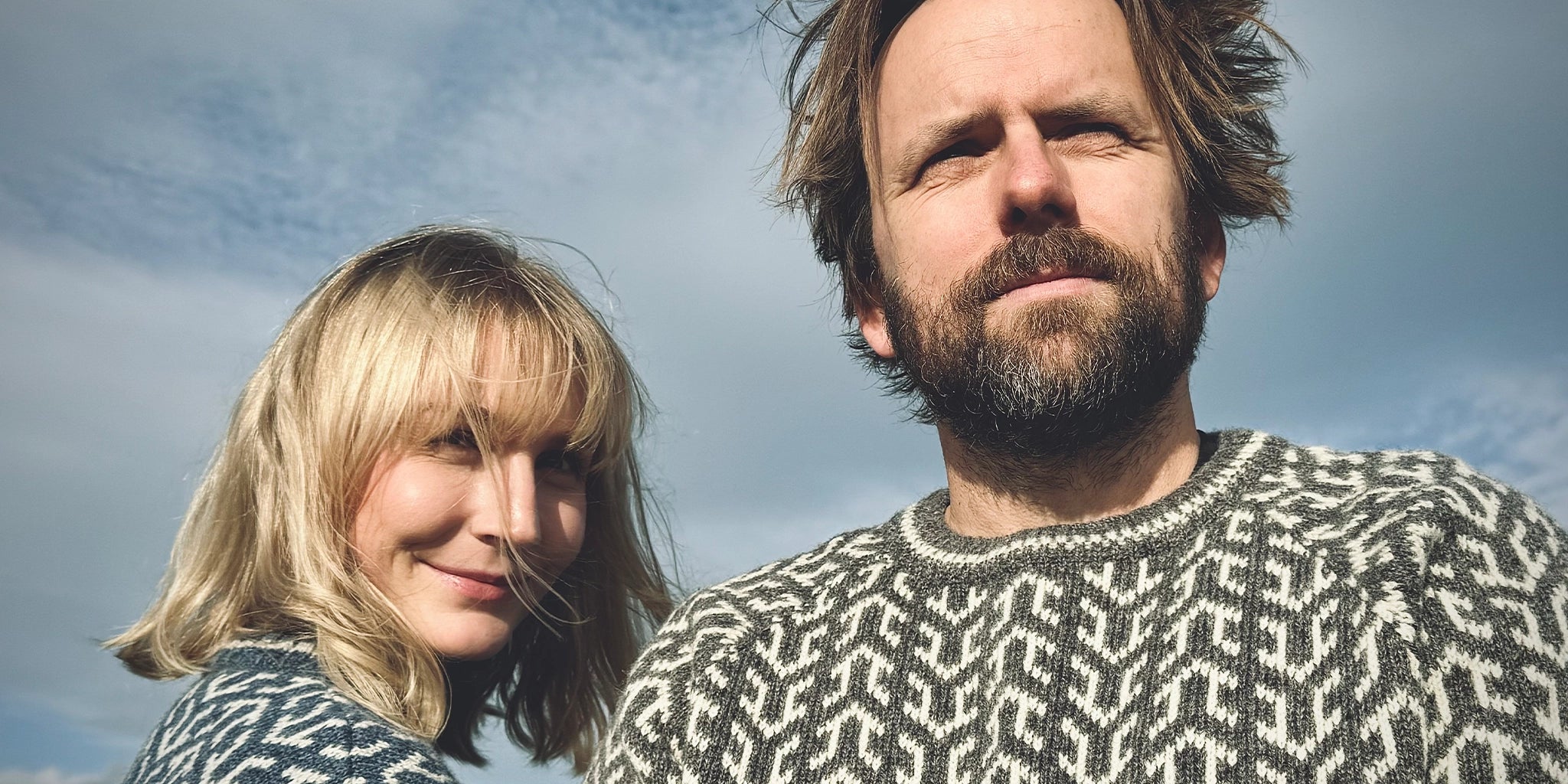 Nærbilde, mann og kvinne i langermede Nordvegr ullgensere fra Vikingstrikk med pilmønster.