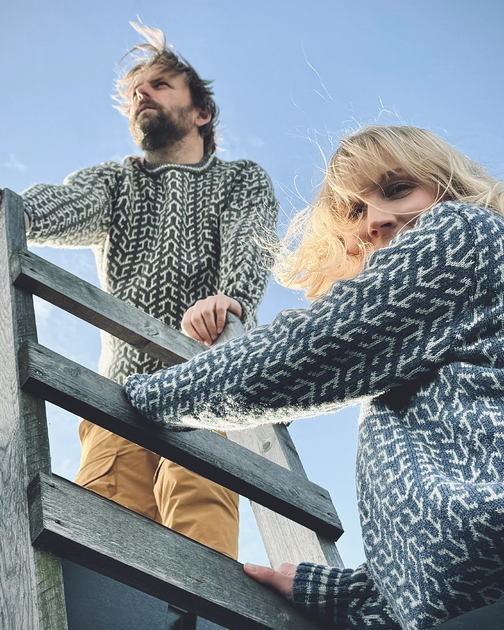 To personer i Nordvegr-gensere fra Vikingstrikk, varme ullgensere med nordisk mønster, fanget i et øyeblikk med naturlig lys og vind.