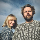 Nærbilde, mann og kvinne i langermede Nordvegr ullgensere fra Vikingstrikk med pilmønster.