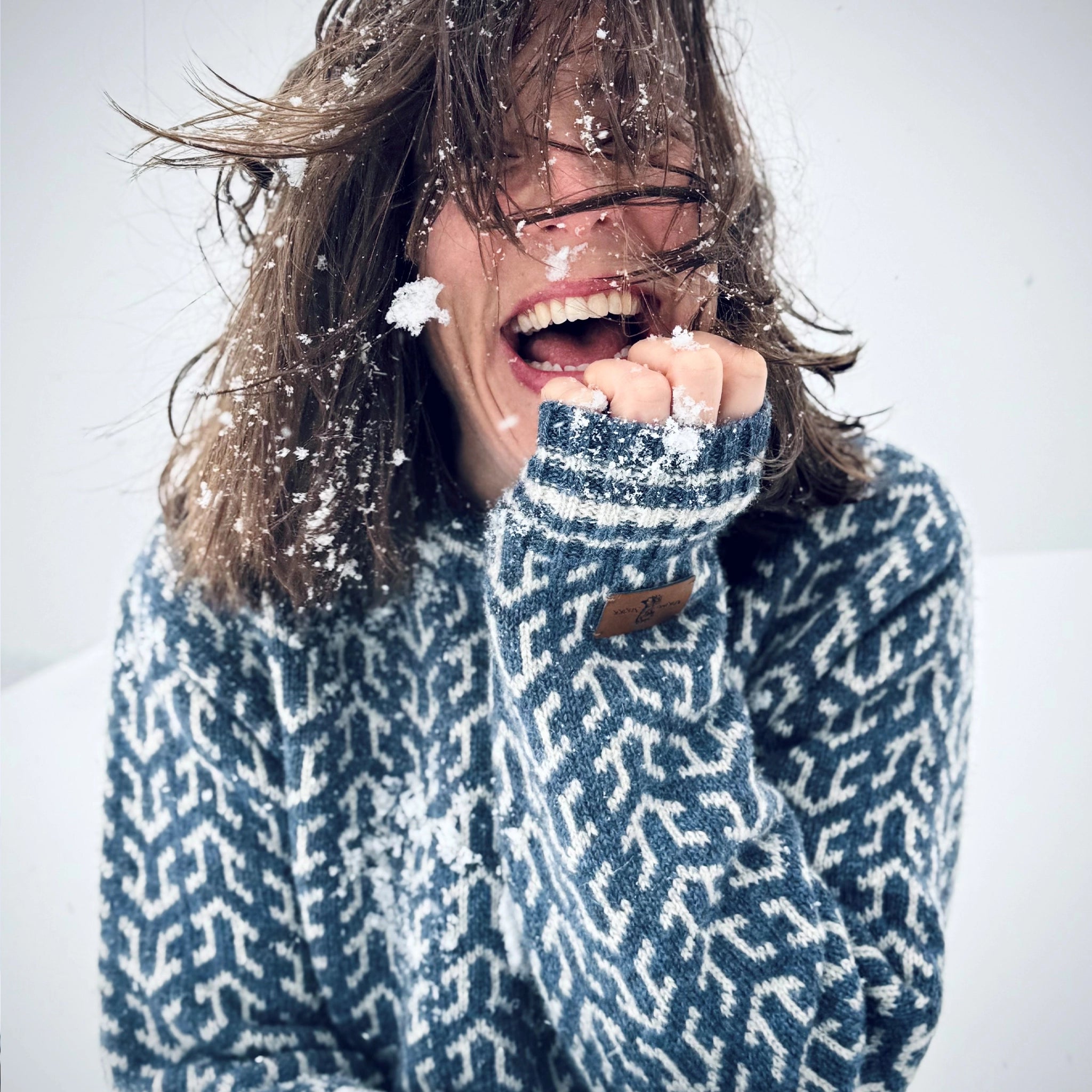 Nærbilde, kvinne med blå Nordvegr ullenser fra Vikingstrikk, ser rett i kameraet og smiler stort.