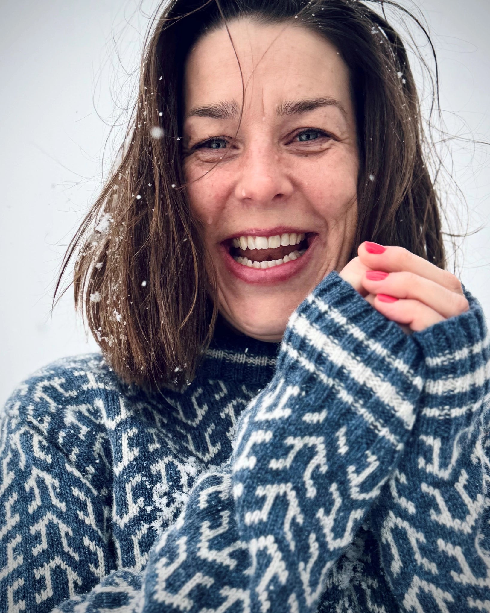 Smilende kvinne i blå og hvit Nordvegr-genser fra Vikingstrikk, en allsidig ullgenser for friluftsliv, lek, utendørs glede og byturer.