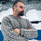 Nærbilde, barsk mann med skjegg i blå Nordvegr ullenser fra Vikingstrikk, ser ut av bildet med armene i kors.
