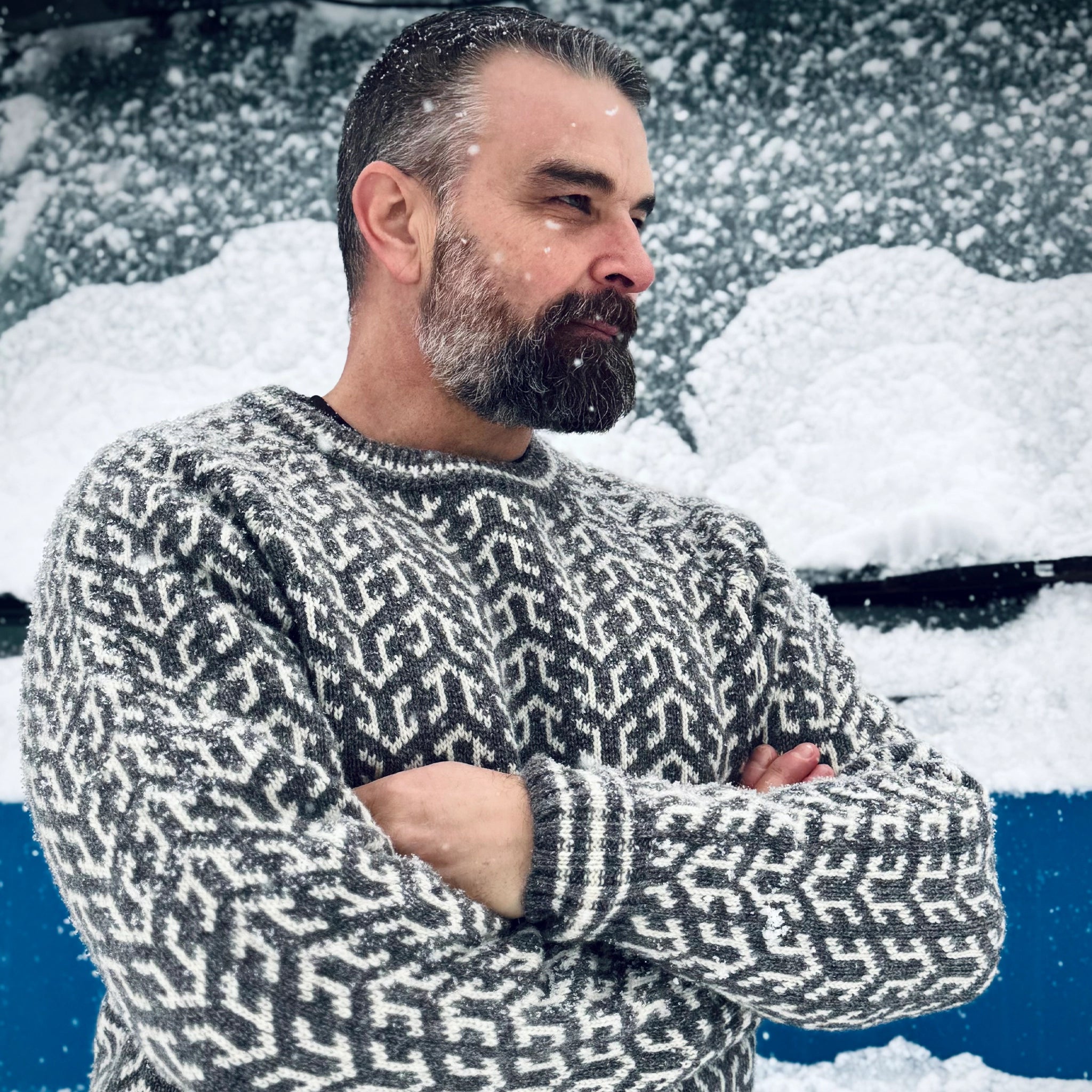 Nærbilde, barsk mann med skjegg i blå Nordvegr ullenser fra Vikingstrikk, ser ut av bildet med armene i kors.