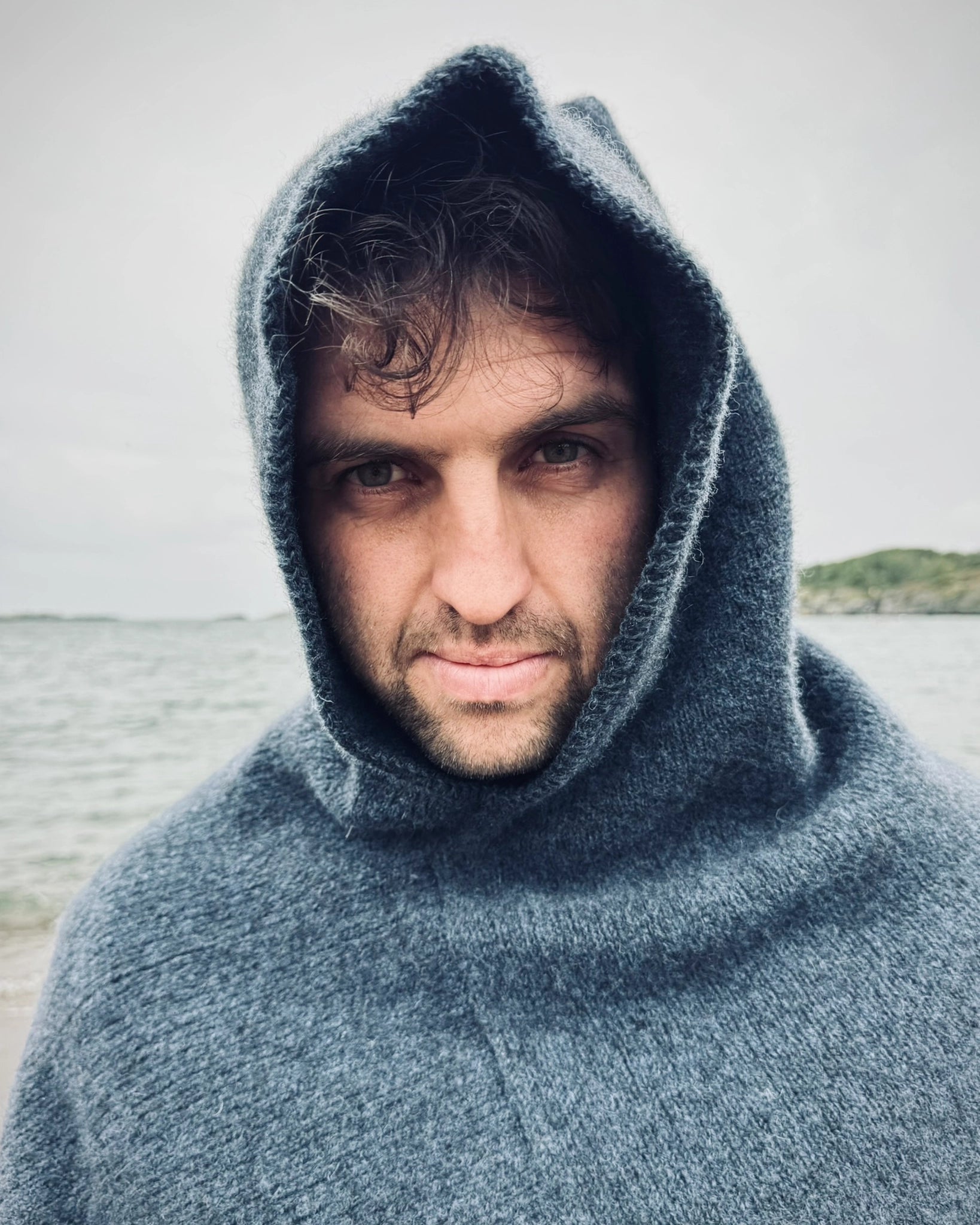 Nært portrett av mann ved sjøen iført mørk blå Vikinghette fra Vikingstrikk, med blikket rettet mot kamera.